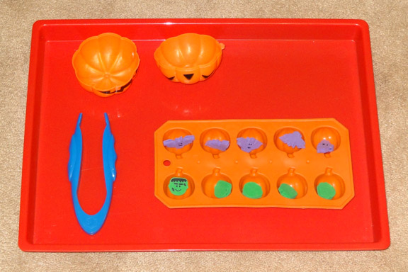 Halloween Montessori activities: Using easy grip tweezers to transfer Halloween-themed erasers into a pumpkin-shaped ice cube tray || Gift of Curiosity