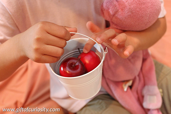 This delightful apple sensory bin invites children to engage in rich dramatic play and to develop their fine motor skills. This is a perfect bin for a preschool apple unit! || Gift of Curiosity