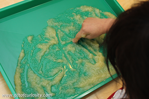 Writing letters in apple sauce. Combine letter learning with sensory play to help preschoolers learn the alphabet. I've gotta try this with my kids! || Gift of Curiosity